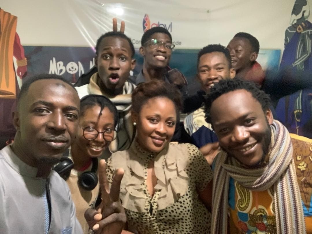 Selfie de groupe dans la salle du studio, devant une affiche de Mboa Matanda.