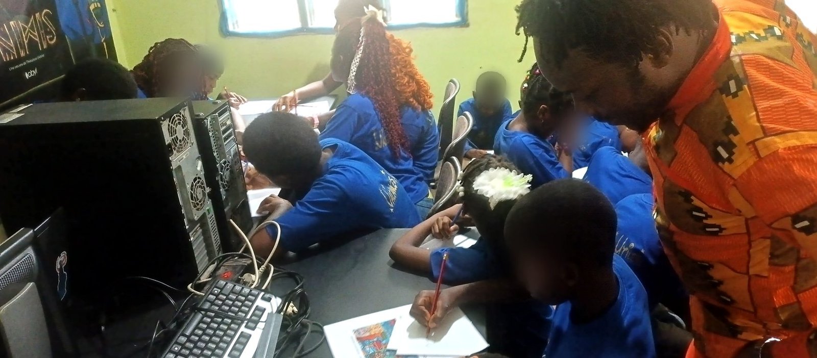 Des enfants dessinent à une grande table pendant que l'intervenant observe.